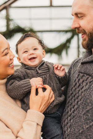 A happy family shares a joyful moment together while wearing cozy knit sweaters in a greenhouse.