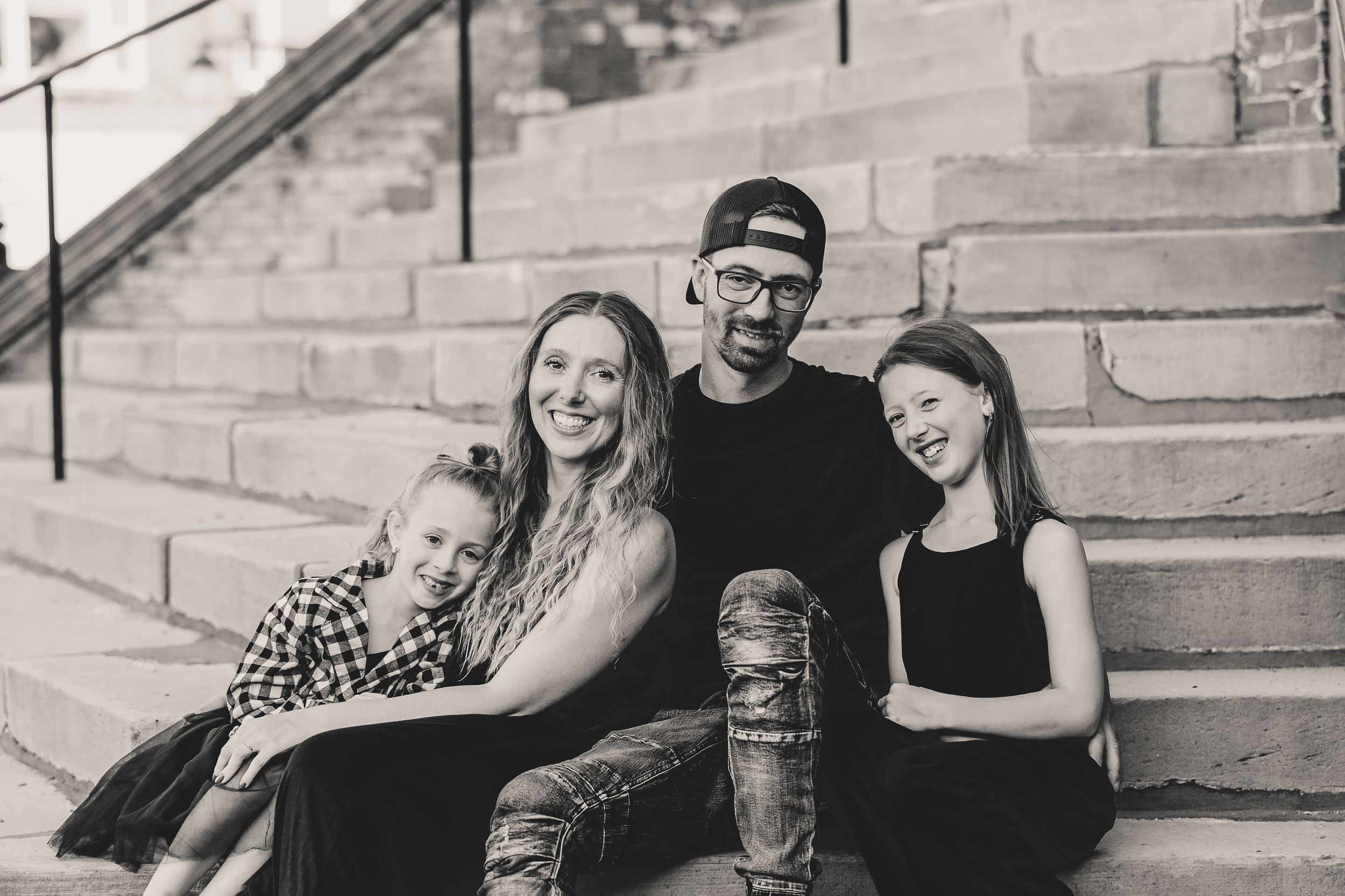 A family of four sitting together on outdoor stone steps, sharing laughter and hugs.