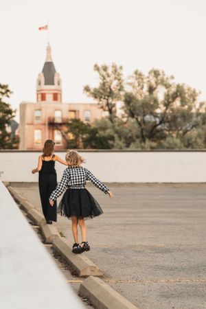 Two children in black and checkered outfits balance on a concrete surface at sunset with an old building spire visible in the background.