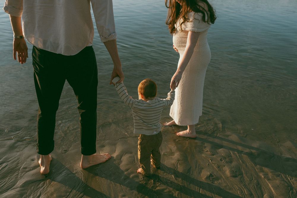 People walking barefoot along the water's edge at sunset.