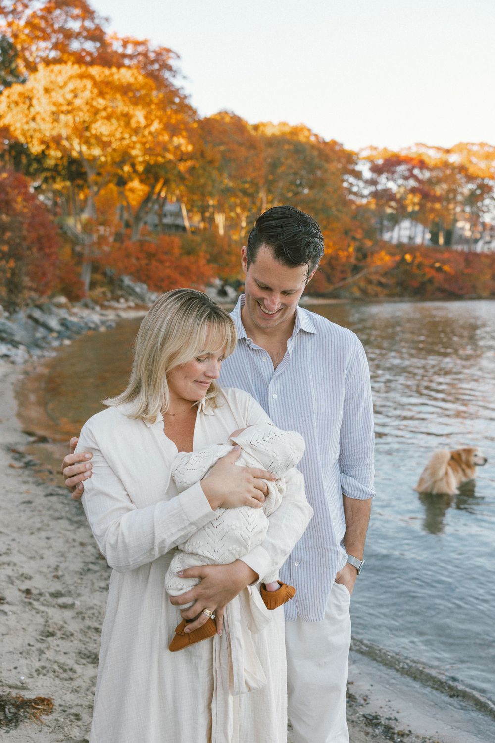 Family in white outfits sharing tender moments by autumn waterfront.