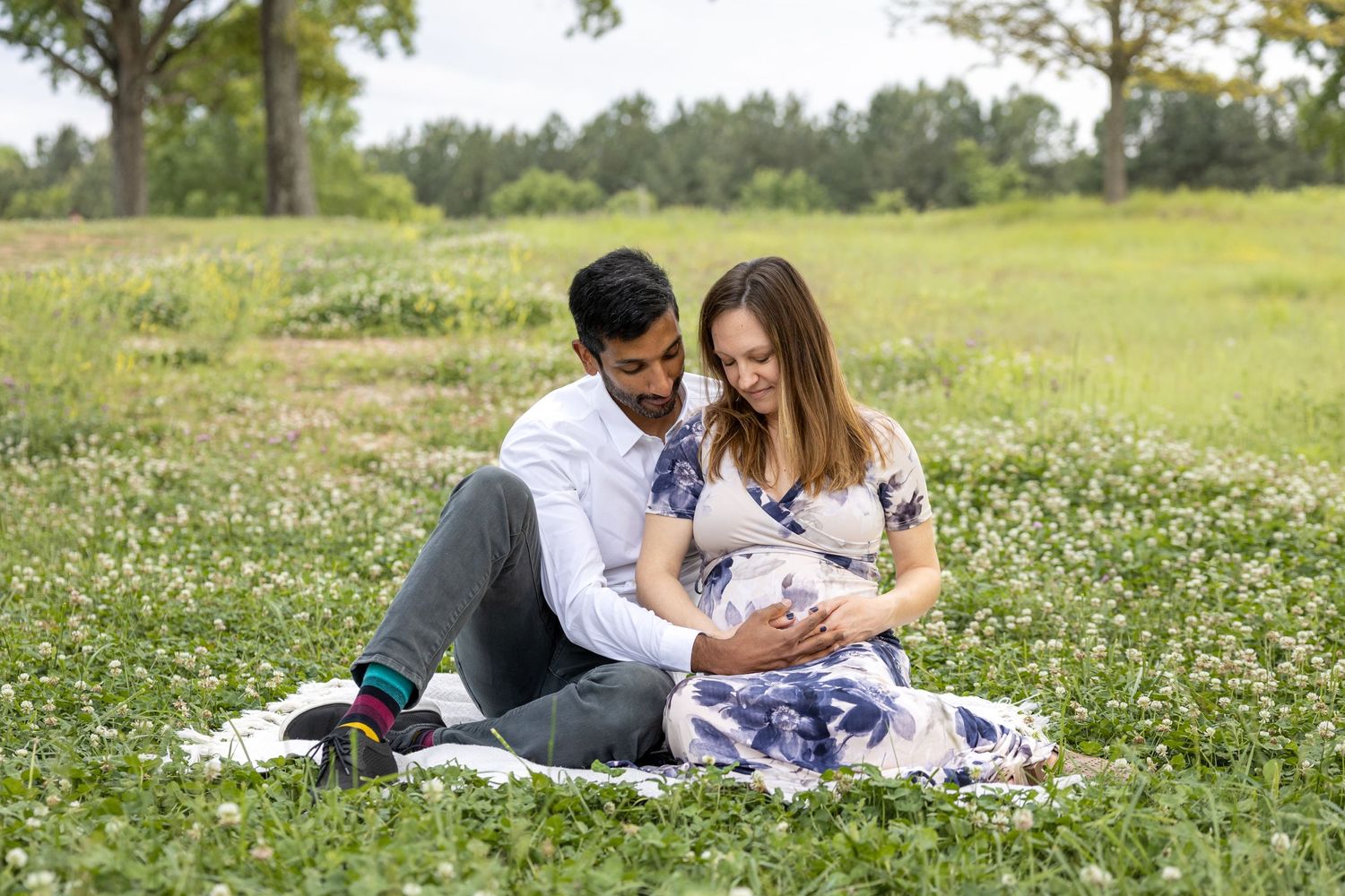 A couple sits in a field of flowers at their Raleigh NC Art Museum maternity photo session.