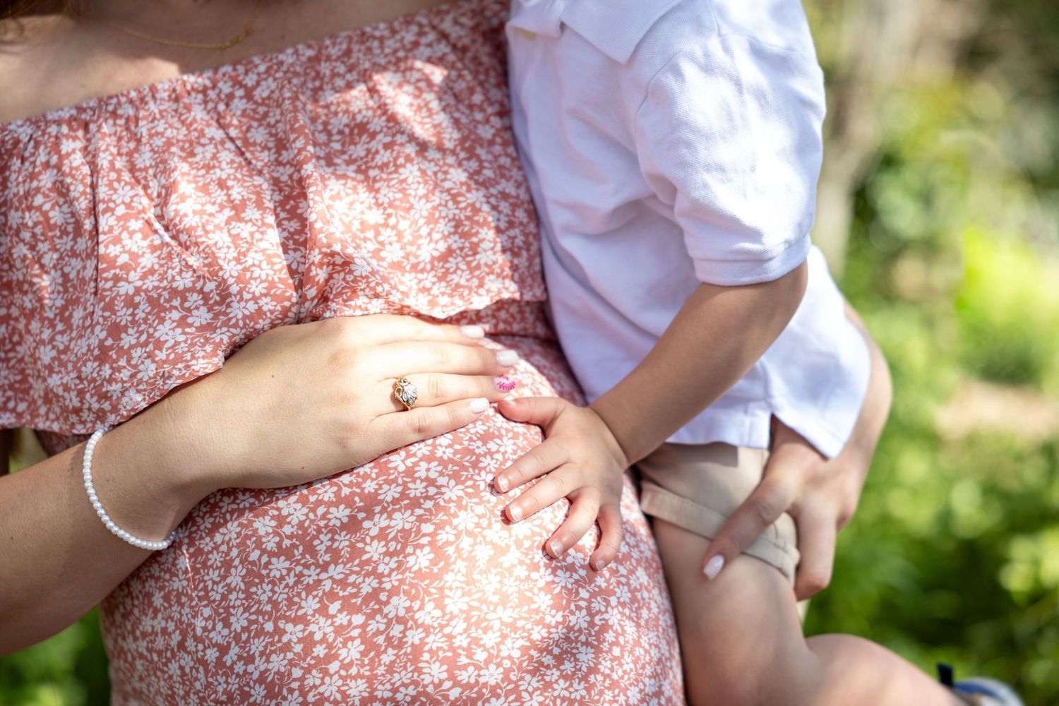 A close up of a baby bump in pink and white dress with a toddler hand.