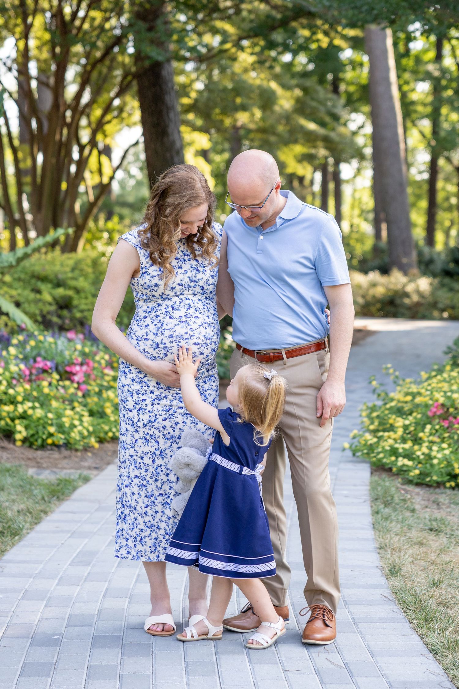 A family with a young toddler reaching up to mom's baby bump gathers on a walking path in Raleigh.