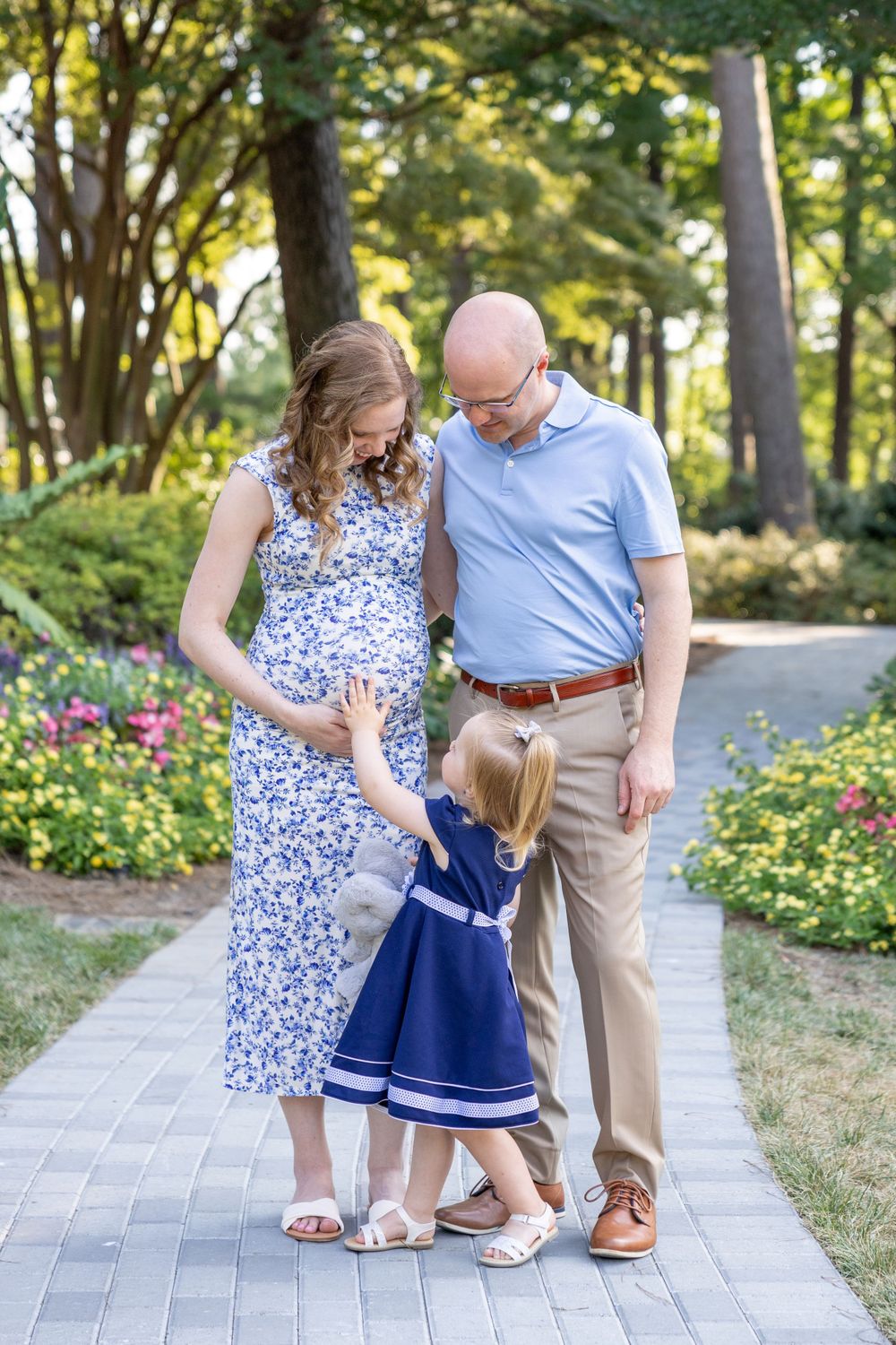 A family with a young toddler reaching up to mom's baby bump gathers on a walking path in Raleigh.