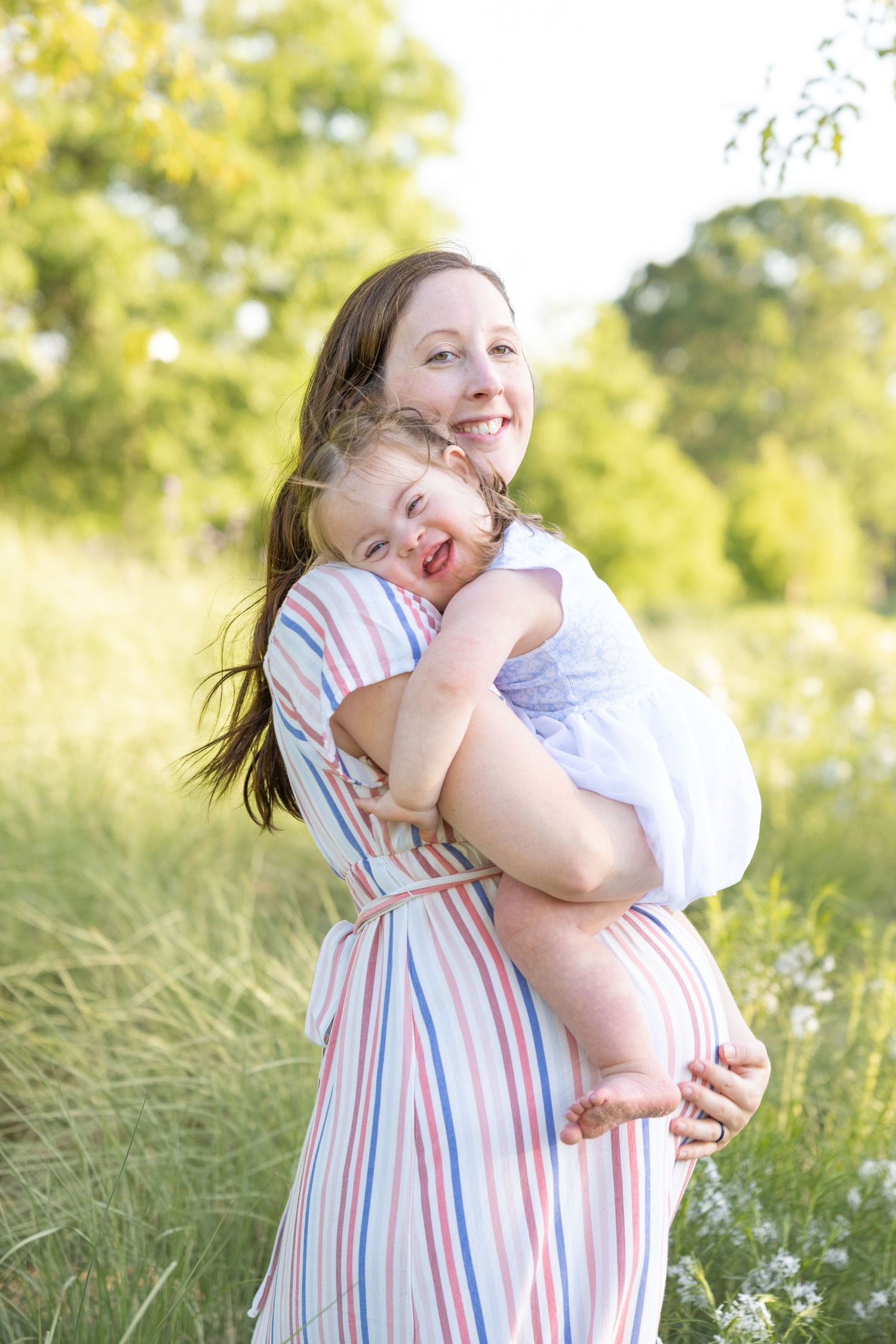 A mom holds her brunette daughter smiling in a field of long grass at the NC Art Museum maternity session..