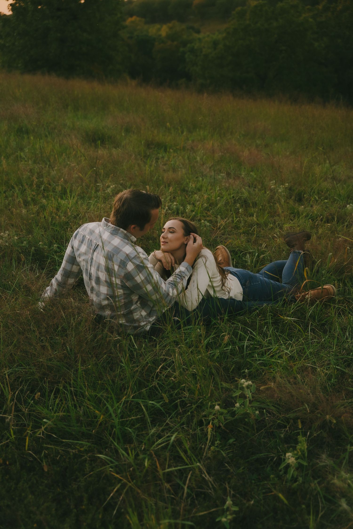 Couple lying in tall grass during golden hour engagement session.