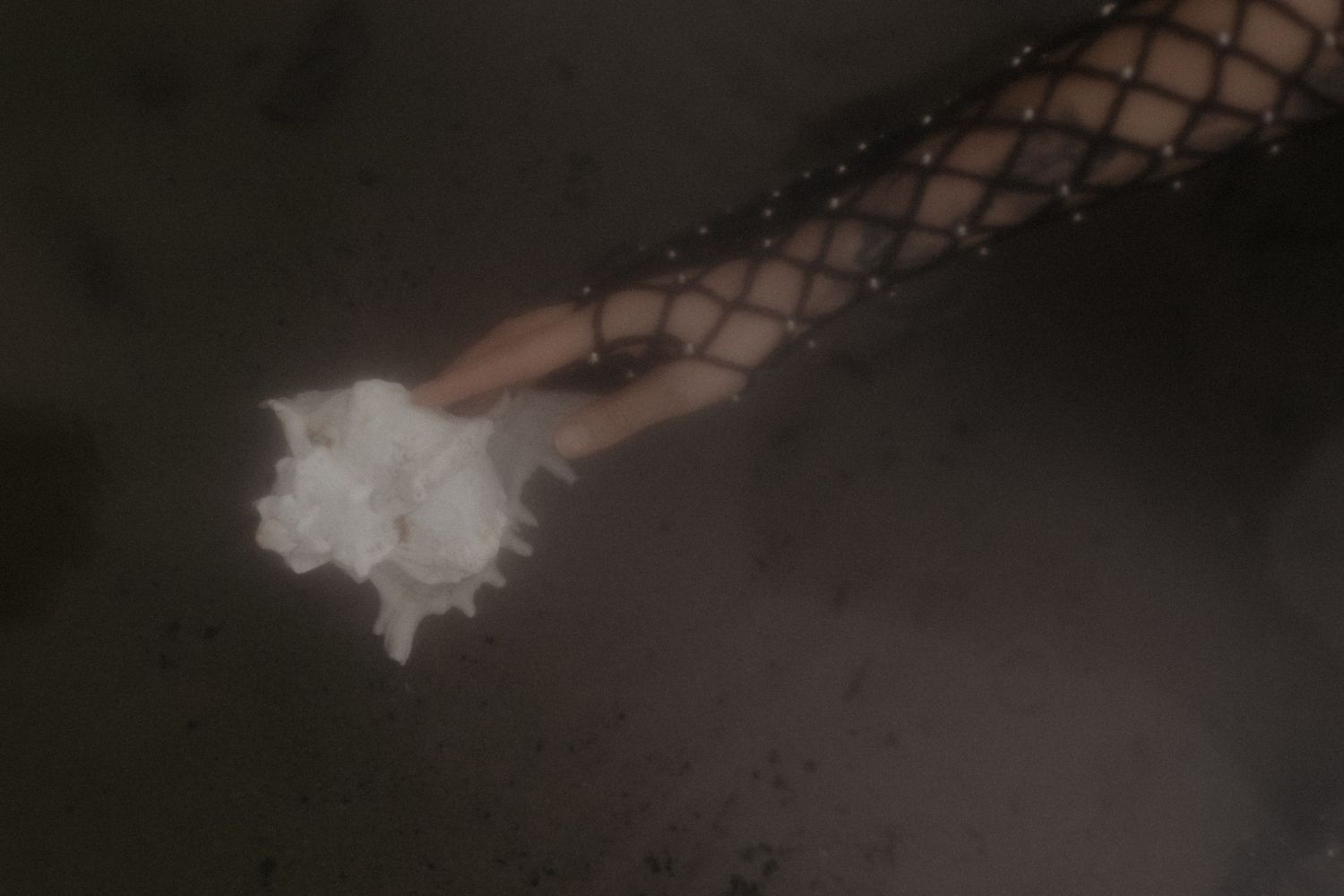 Artistic close-up of arm wearing fishnet sleeve with mystical smoke effect against dark background.