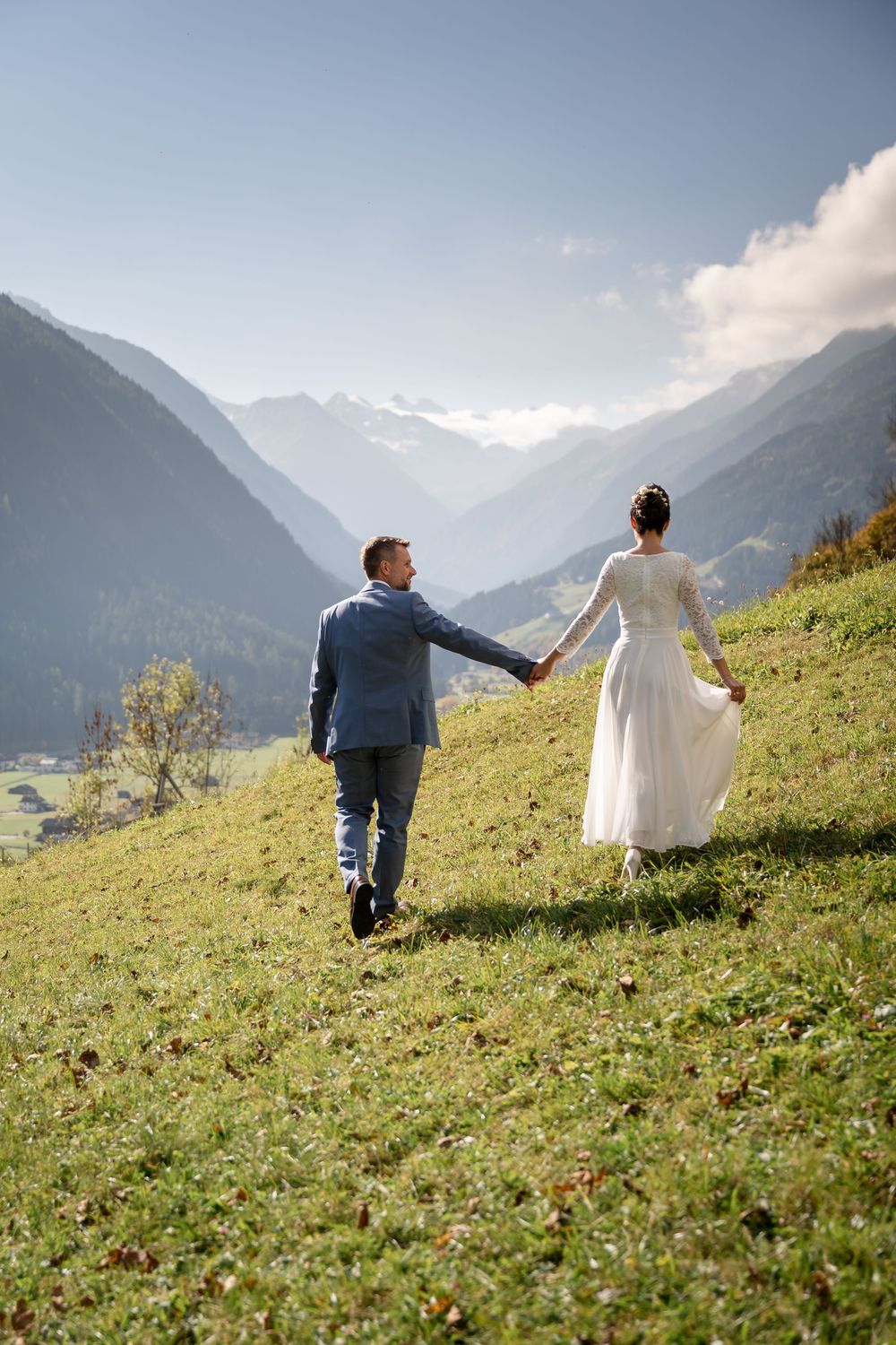 Brautpaar geht Hand in Hand über eine Alm mit Panoramablick auf die Berge des Stubaitals