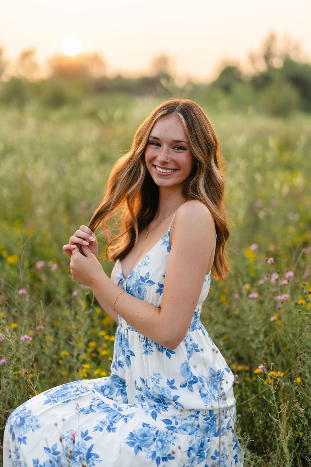 A person in a white and blue floral dress poses joyfully in a wildflower meadow at golden hour.