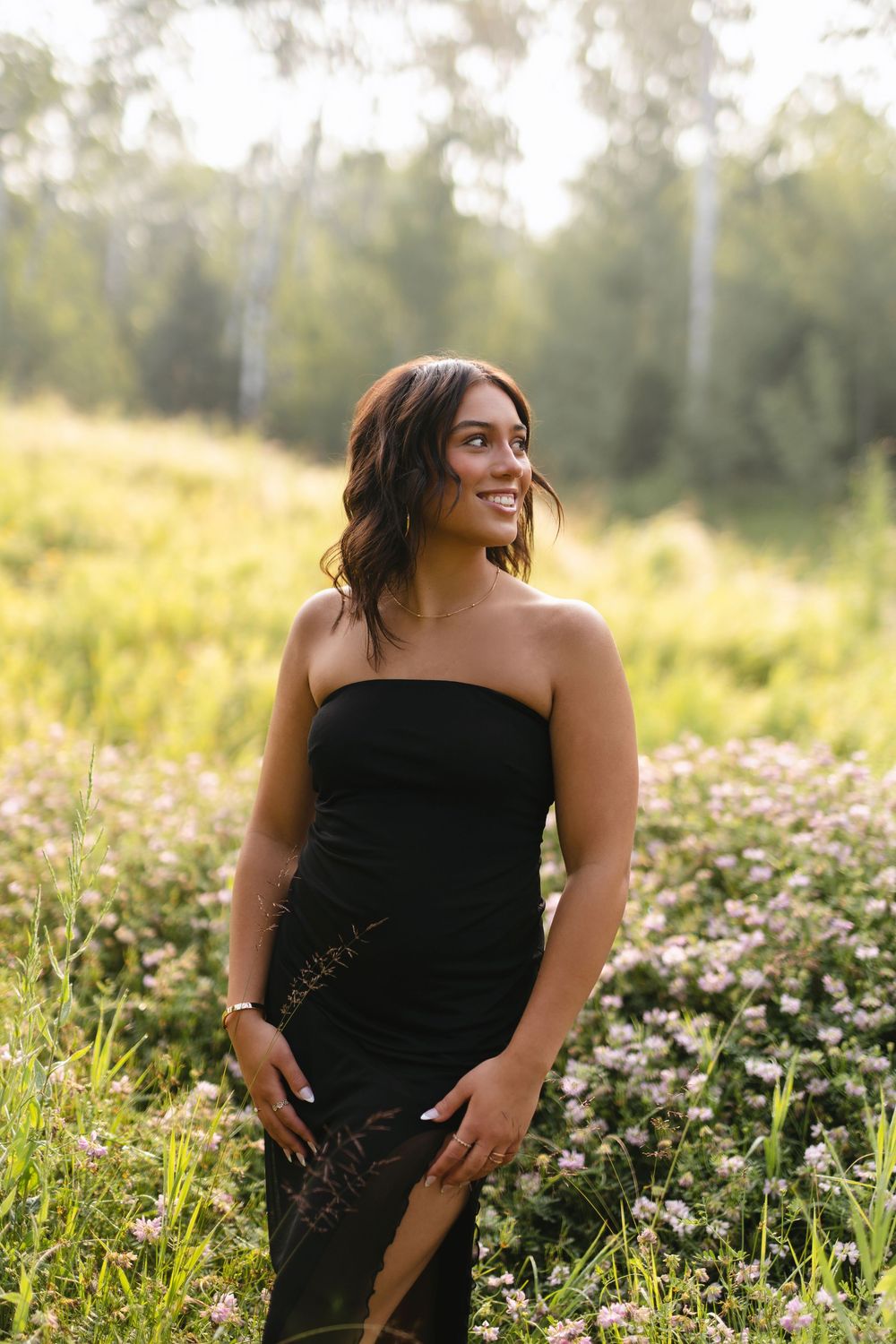 A person in a black dress poses in a sunny wildflower meadow during golden hour.