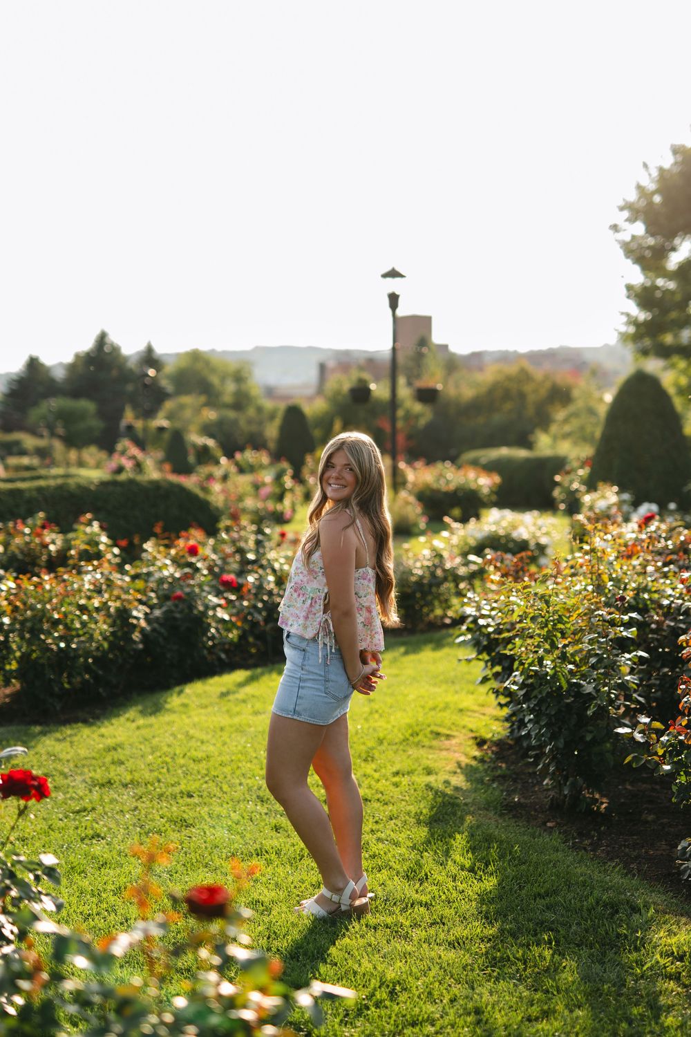 A person walks through a vibrant flower garden filled with colorful blooms on a sunny summer afternoon.