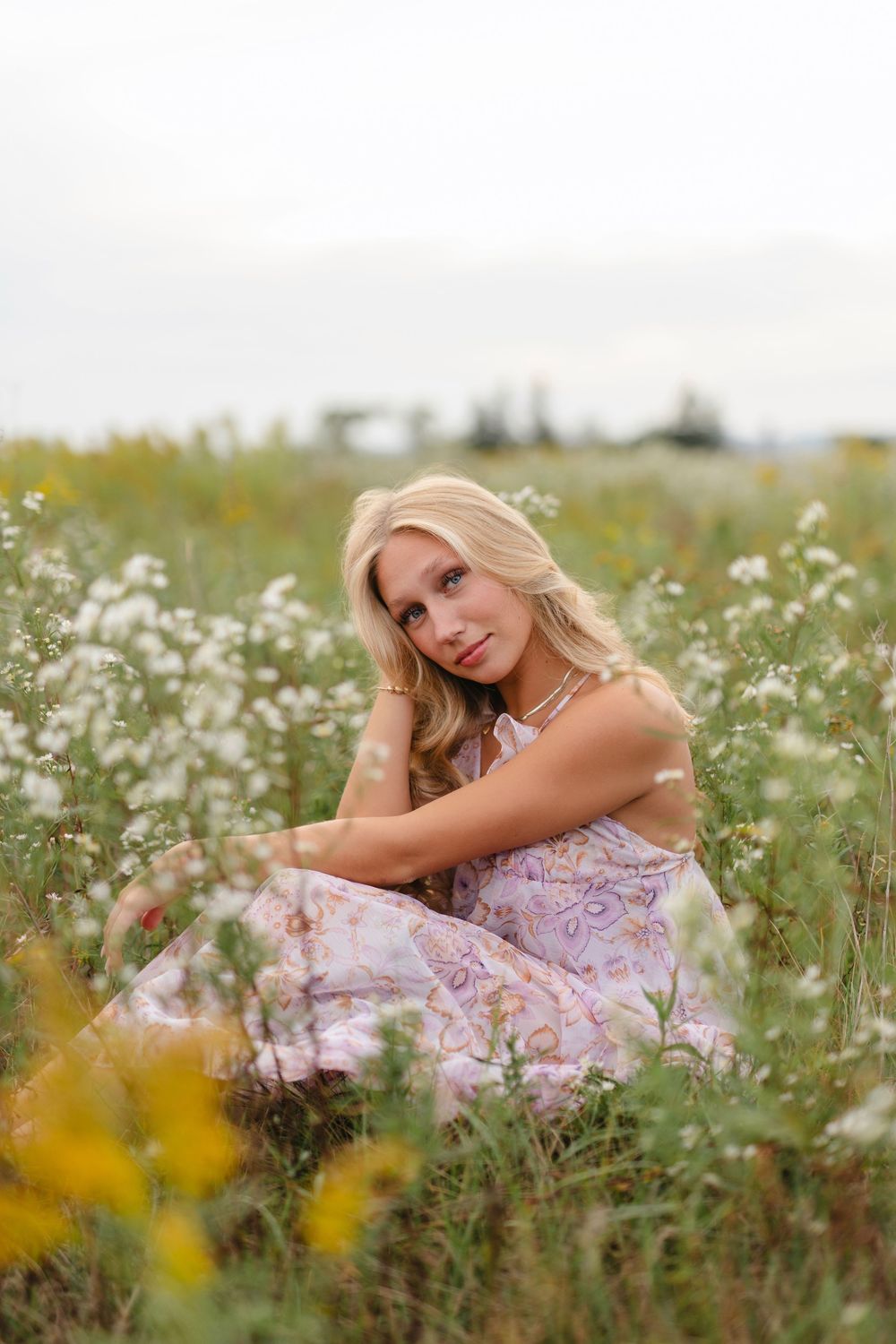 A person in a pink floral dress poses gracefully among wildflowers in a sunny meadow.