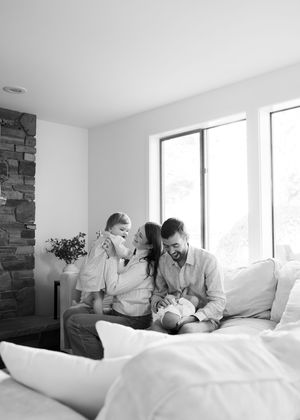 A family shares joyful moments together on a white couch near large windows.