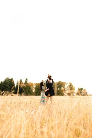 A couple stands together in a golden wheat field during sunset.