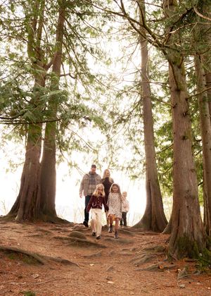A family walks together on a forest trail surrounded by towering evergreen trees.