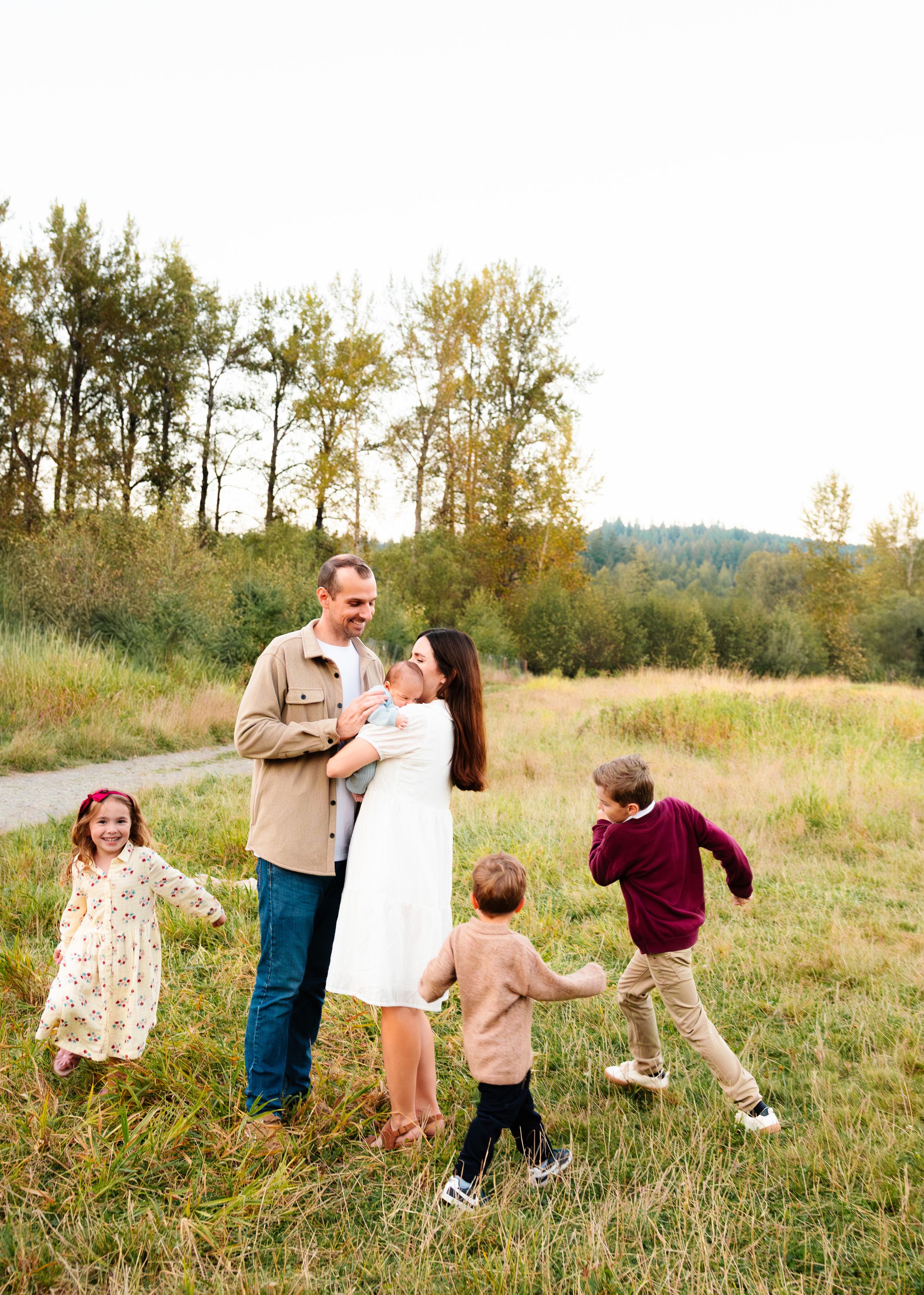 A family plays and dances together in a grassy field during golden hour.