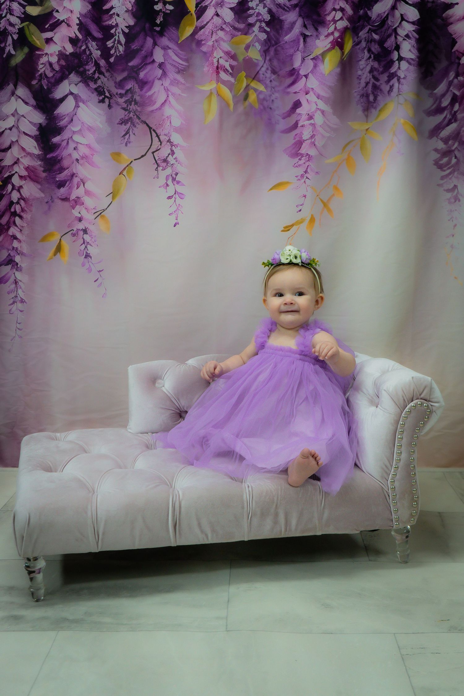 Purple wisteria backdrop with white chaise lounge in dreamy portrait setting.