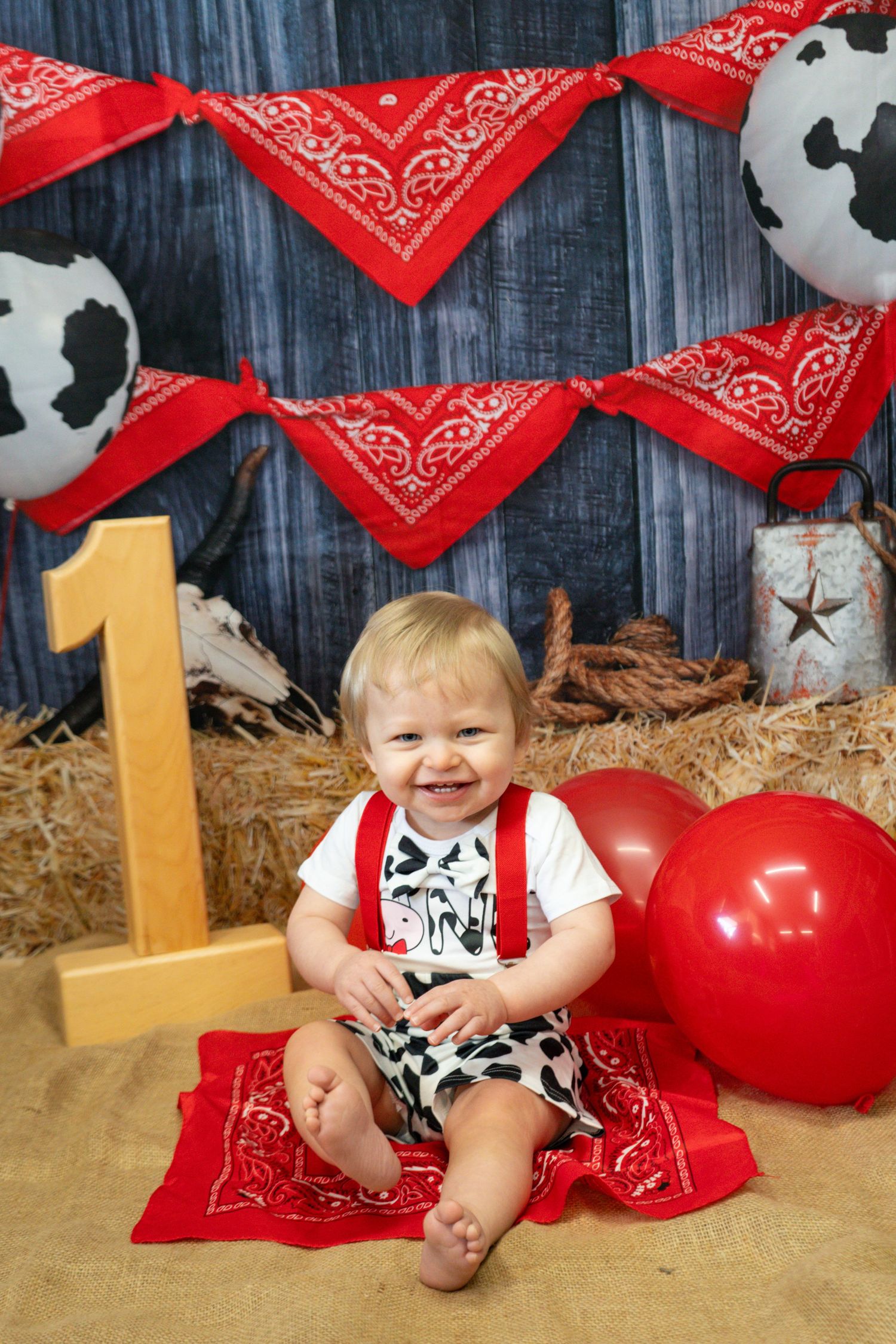 A first birthday cowboy themed photo with red bandanas and cow print decorations.