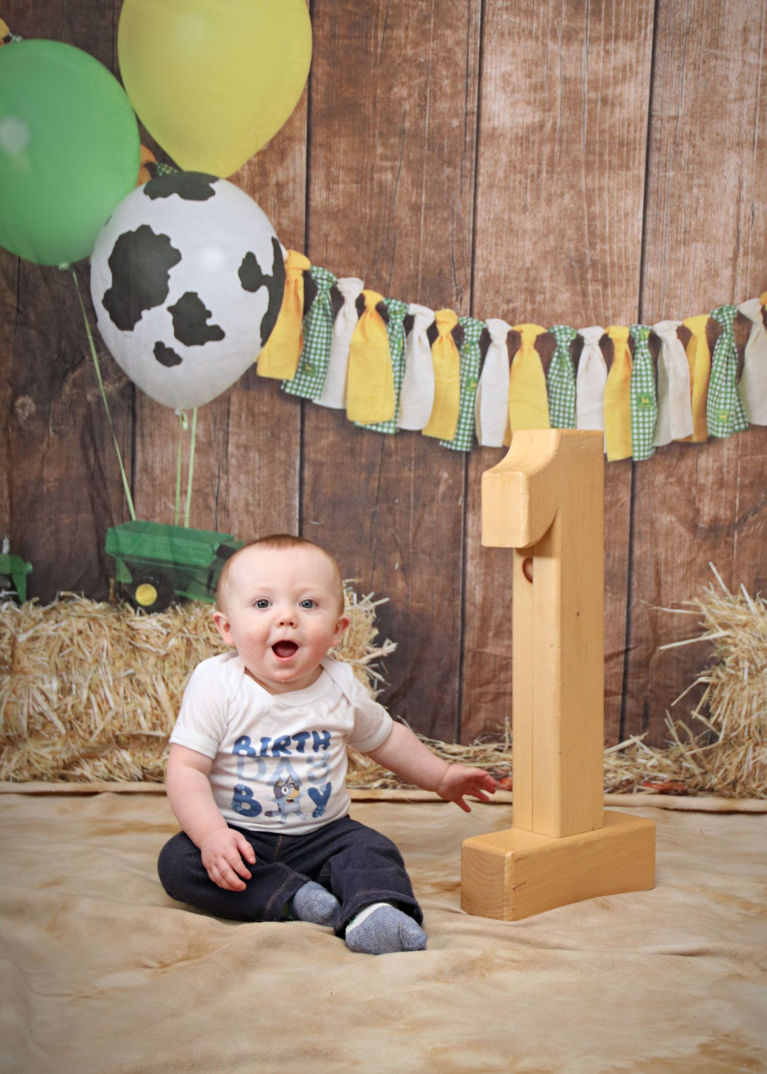 Farm themed first birthday setup with green and yellow decorations and cow print balloons.