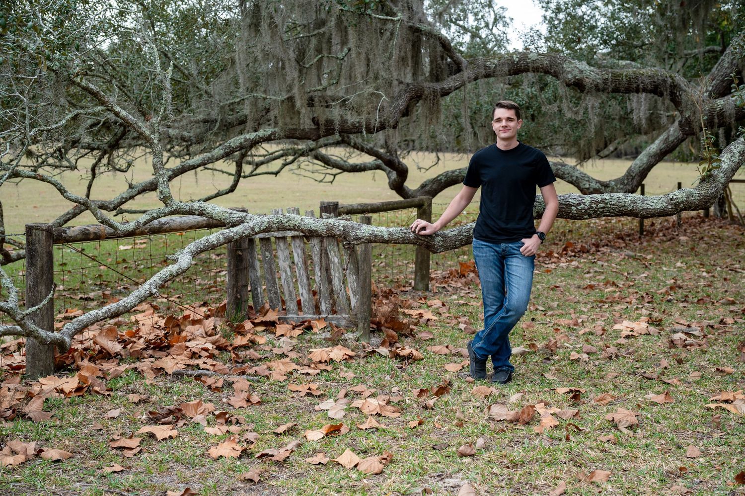 An image of someone standing by a tree trunk in a wooded area with autumn leaves on the ground.