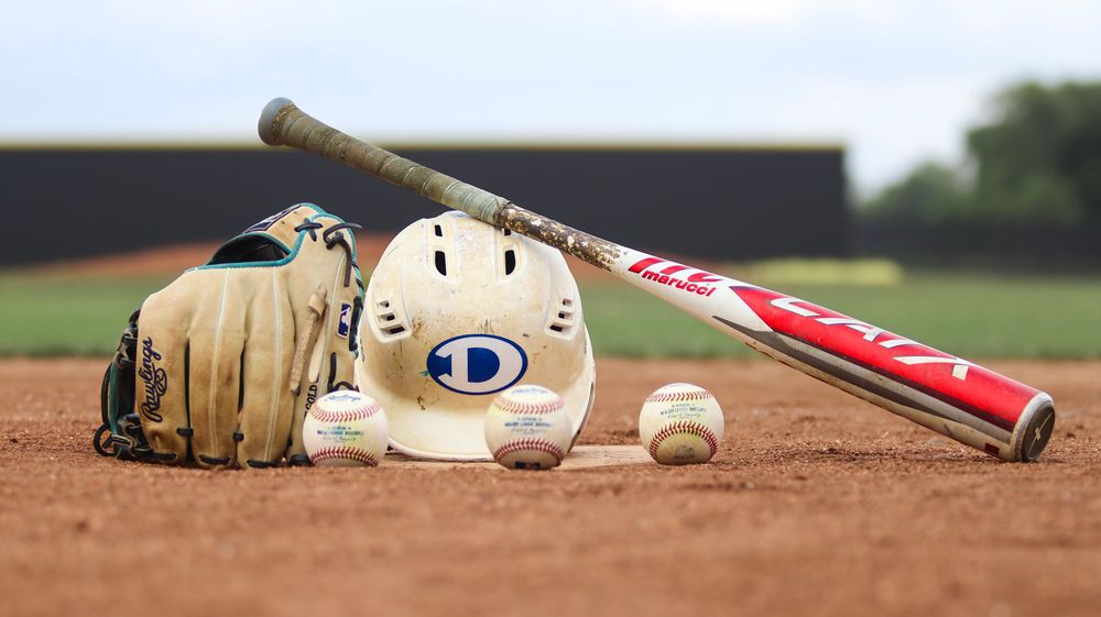 Baseball equipment including bat, glove and ball laid out on infield dirt.