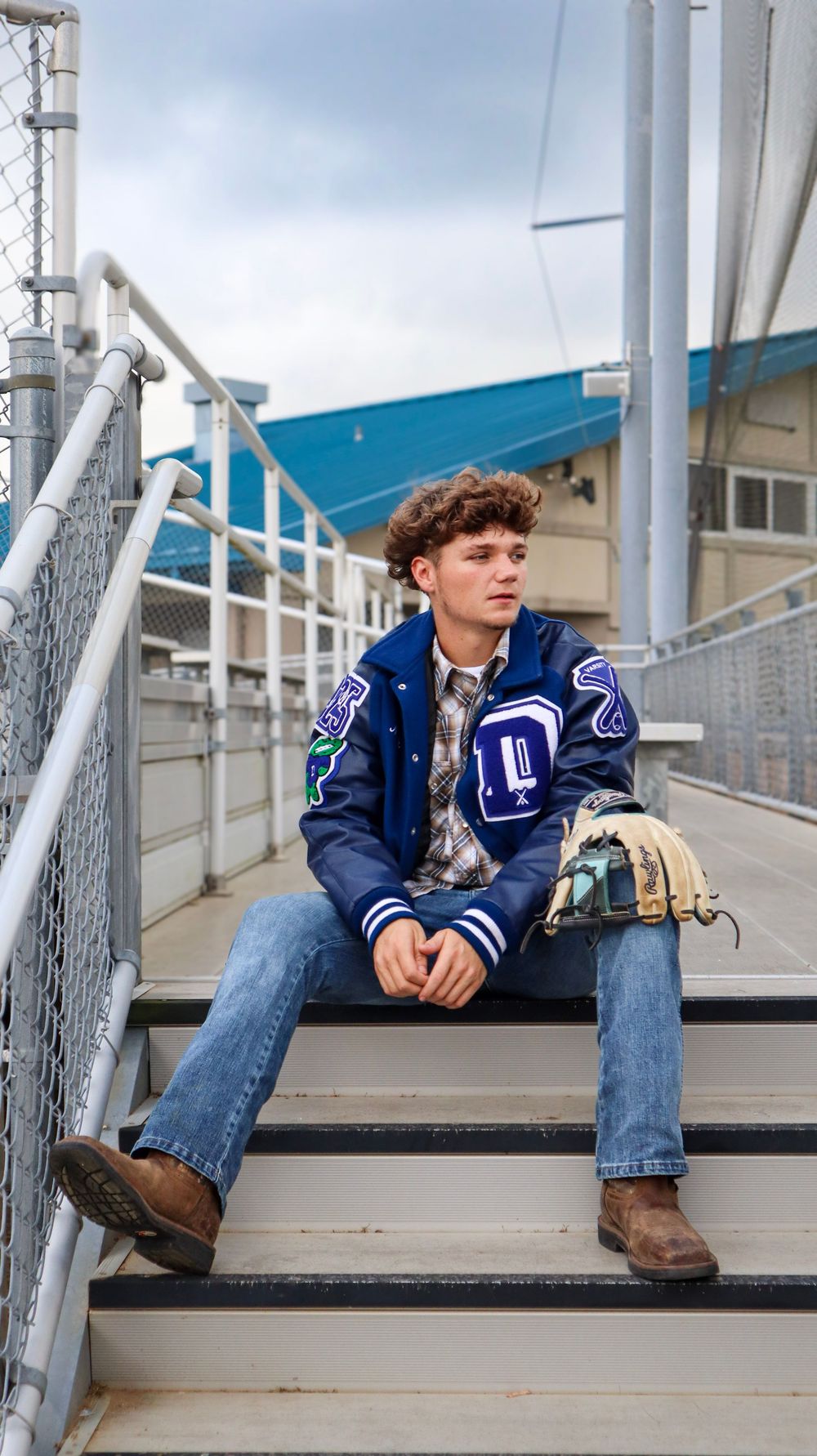 Baseball player in team jacket sitting on bleacher steps at stadium.