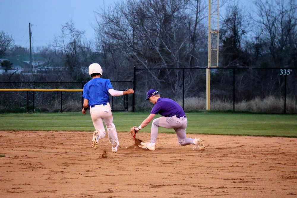 Baseball players practicing sliding techniques on the infield dirt.