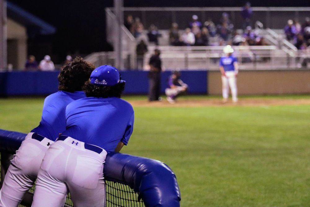 Players in blue uniforms resting along the dugout fence during a baseball game.