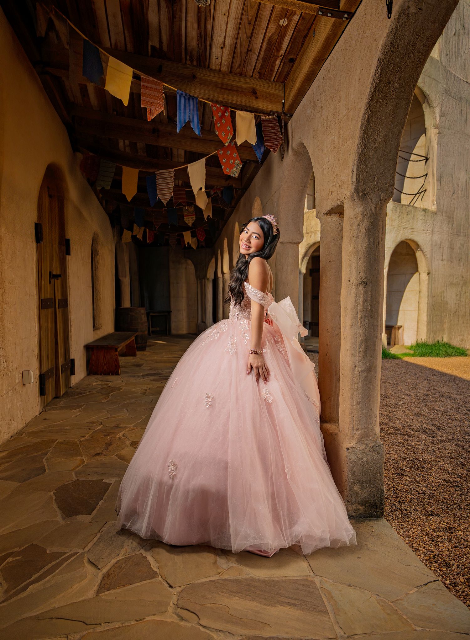 A pink ballgown dress photographed in a rustic stone archway corridor with dramatic lighting and shadows.