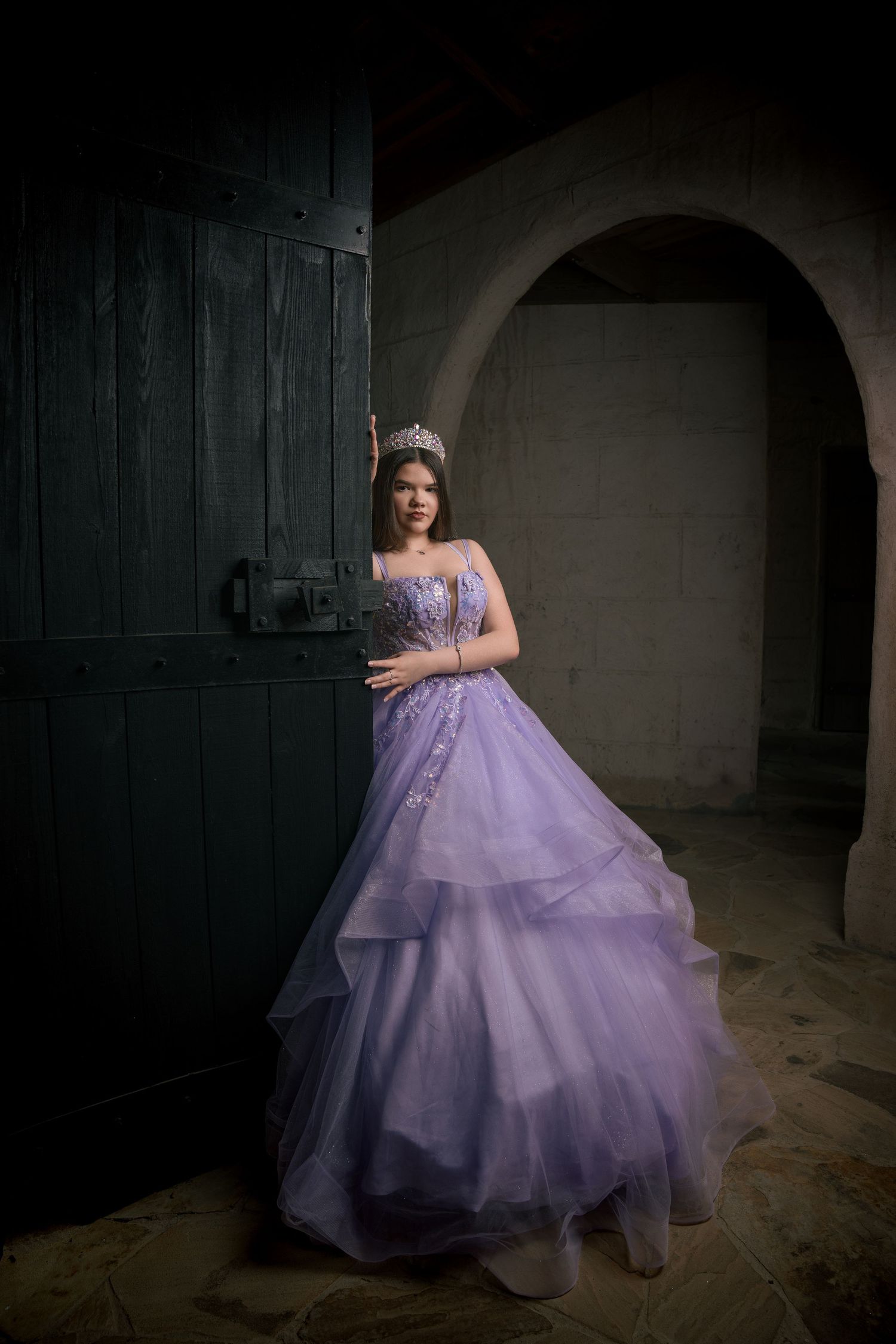 Dramatic castle photoshoot featuring flowing purple princess ball gown in dim lighting.