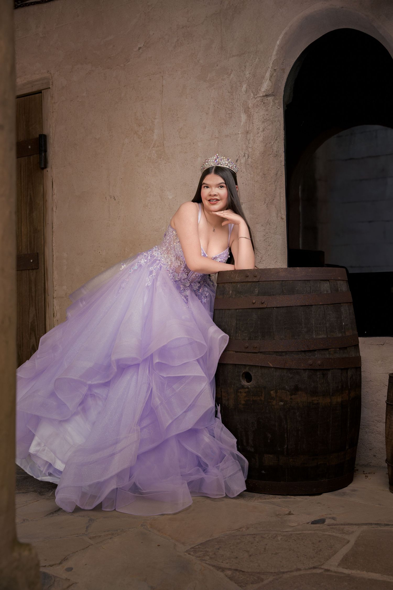 Elegant purple ball gown photo session with rustic wooden barrels in castle setting.