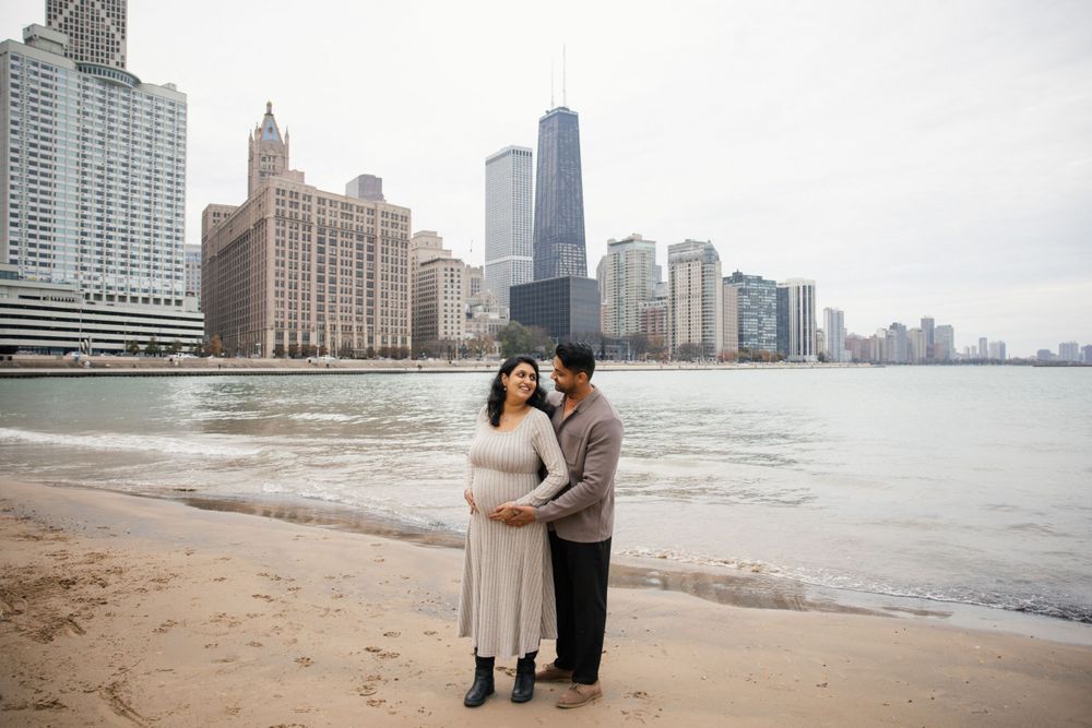 Couple embracing on a beach with Chicago skyline and Lake Michigan in background on cloudy day.