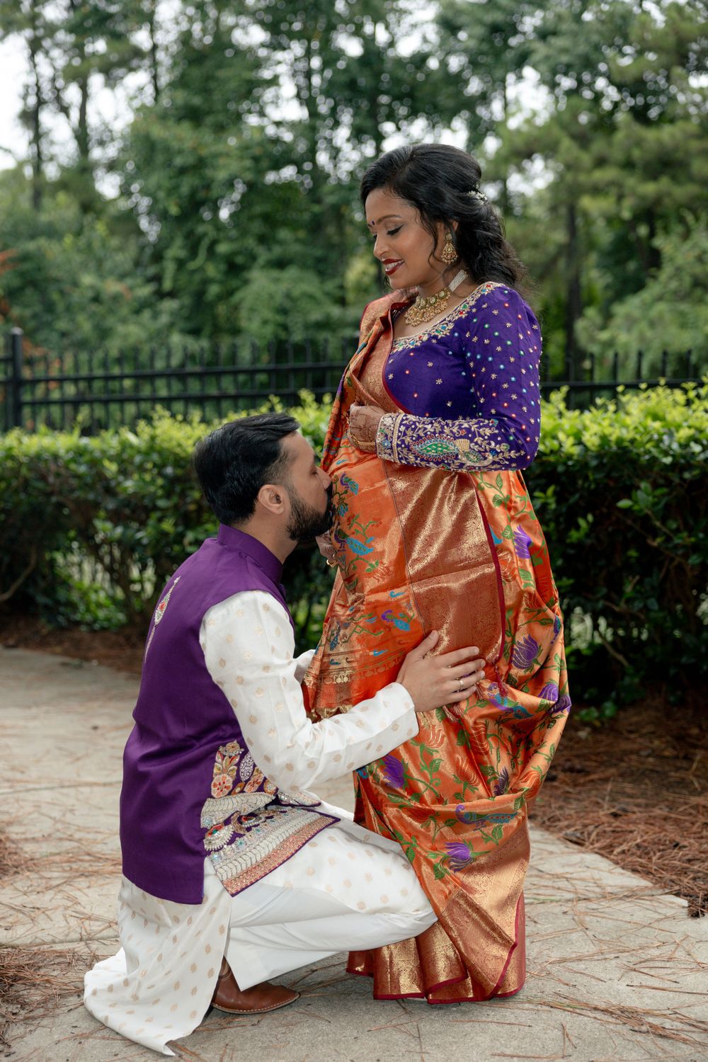 A couple in traditional South Asian attire shares a romantic moment in a garden setting.