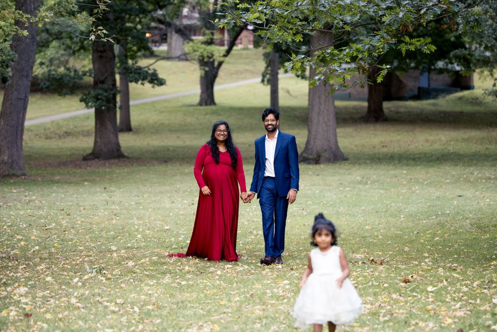 Family in formal attire standing together on grass under tall trees in a park.
