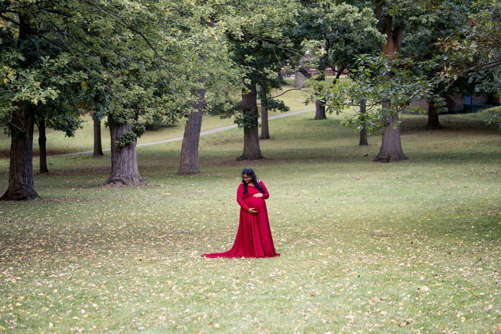 A person wearing a dramatic red dress stands solitary in a tranquil wooded park setting.