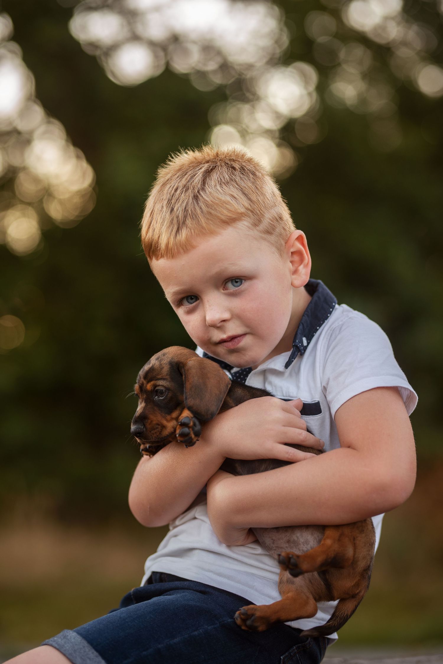 Child hugs small dachshund puppy during outdoor portrait session.