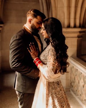Romantic embrace captured in gothic hallway with bride in embellished gown and traditional red bangles.
