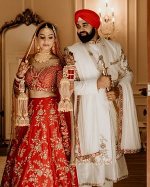 Traditional Punjabi wedding couple in red lehenga and white sherwani with gold embroidery.