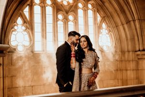 Couple shares joyful moment in gothic architecture hallway with arched windows.