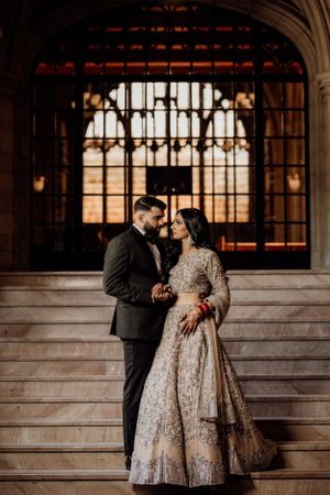 Romantic wedding portrait features couple embracing on historic stone staircase with gothic architecture.