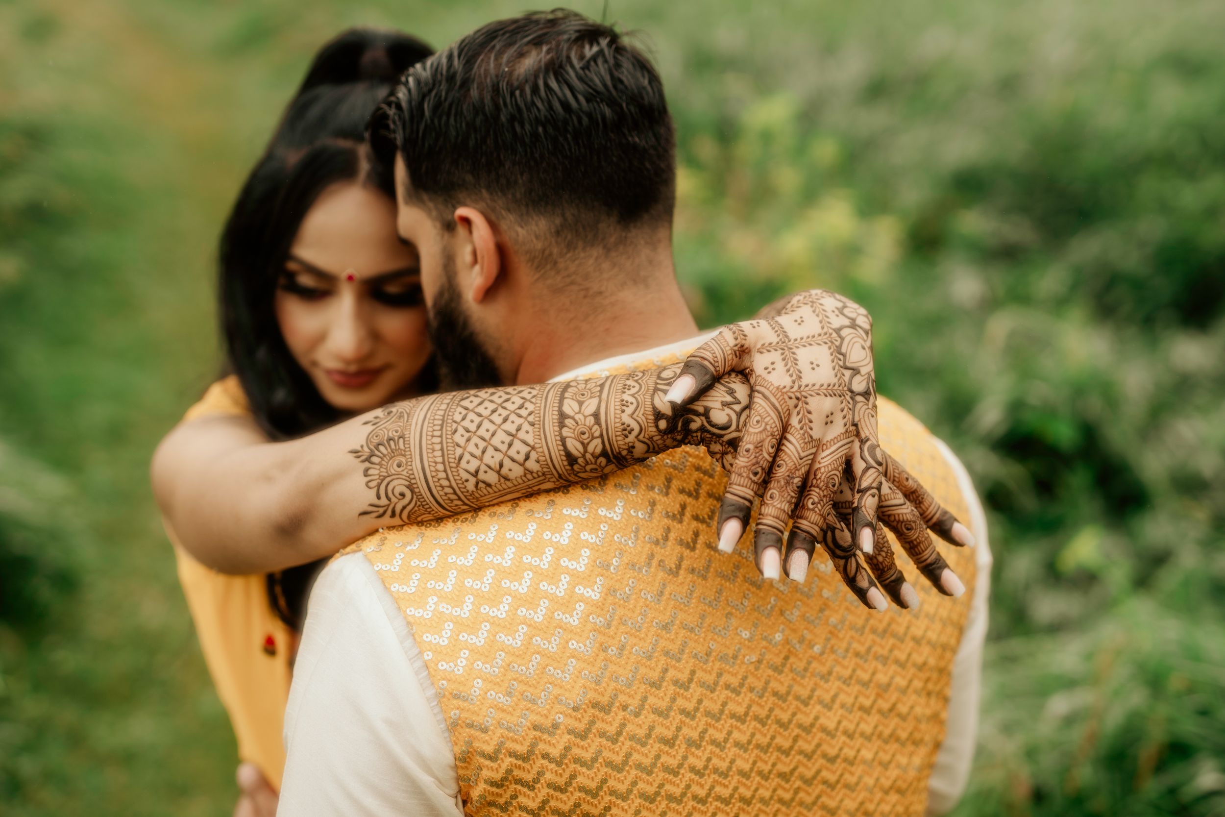 Intimate embrace showing detailed henna artwork against natural outdoor setting.