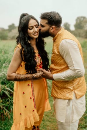 Tender moment in traditional Indian attire amidst green natural backdrop.