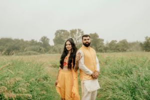 Couple wearing coordinated yellow and white ethnic wear standing in a lush green meadow.