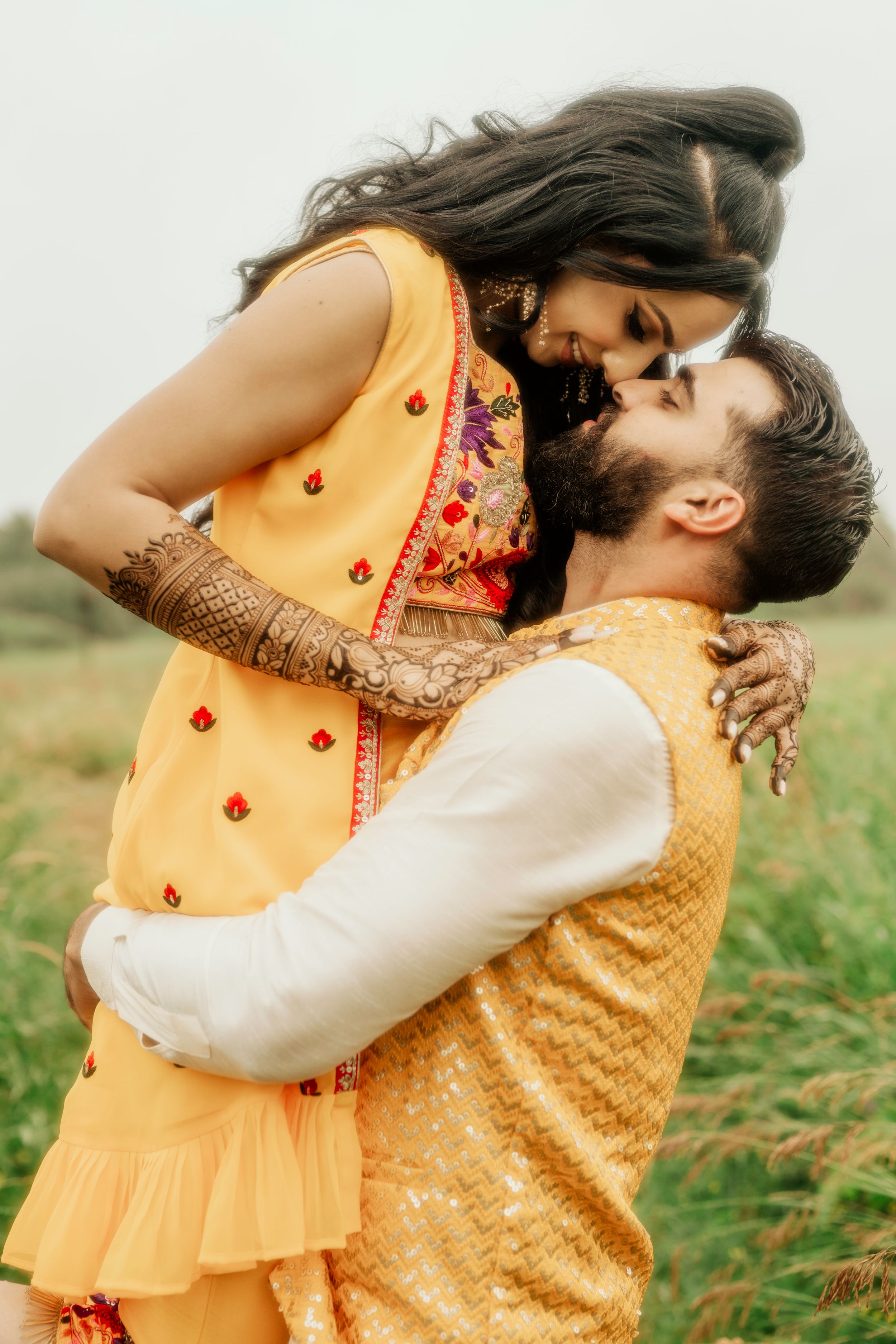 Romantic couple in yellow traditional Indian outfits embrace in a grassy field.