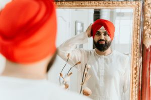 Reflection in mirror showing traditional Sikh attire with bright red turban and white clothing.