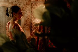 Atmospheric side profile shot of bride in traditional attire with ornate backdrop.