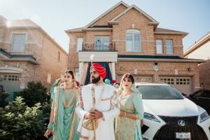 Traditional South Asian wedding scene outside brick house with bridal party in mint green attire.