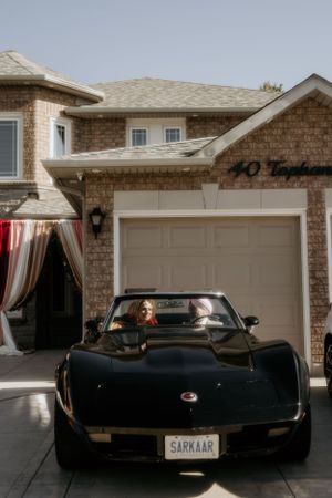 Black vintage Corvette parked in front of a brick house driveway.