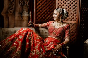 Ornate red bridal lehenga photographed against wooden lattice background in warm lighting.